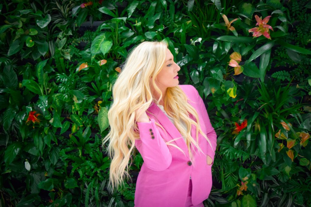 woman in lilac jacket with blonde hair looking up at the hedge