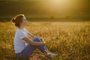 Girl with eyes closed meditating sitting down in a field of corn