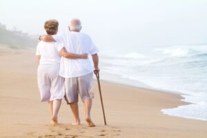 Elderly couple walking on the beach with arms around each other, showing intimacy and connection without sexual focus